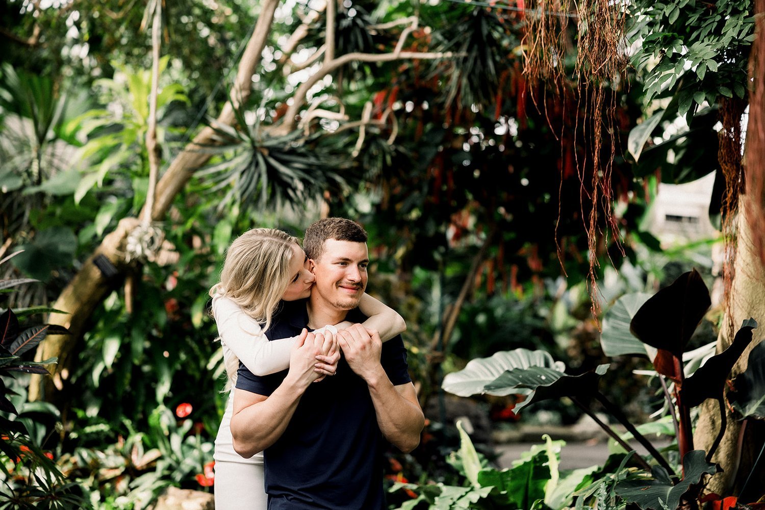 Woman hugging man from behind in front of green tropical plants at Bloedel Conservatory Vancouver, BC