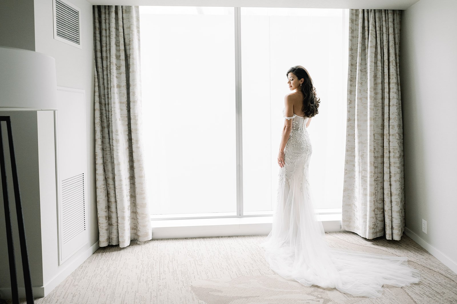 Bride stands in front of window, gets ready at JW Marriot Parq Vancouver for wedding