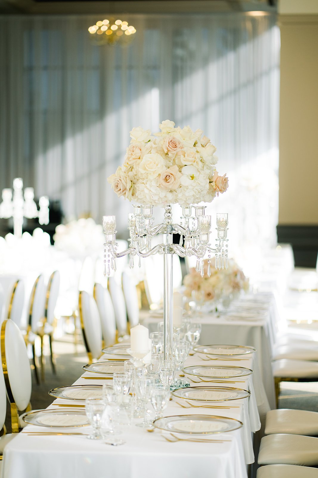 Pink and white floral centrepiece in tall stands amid golden place settings on reception table at Swaneset.  