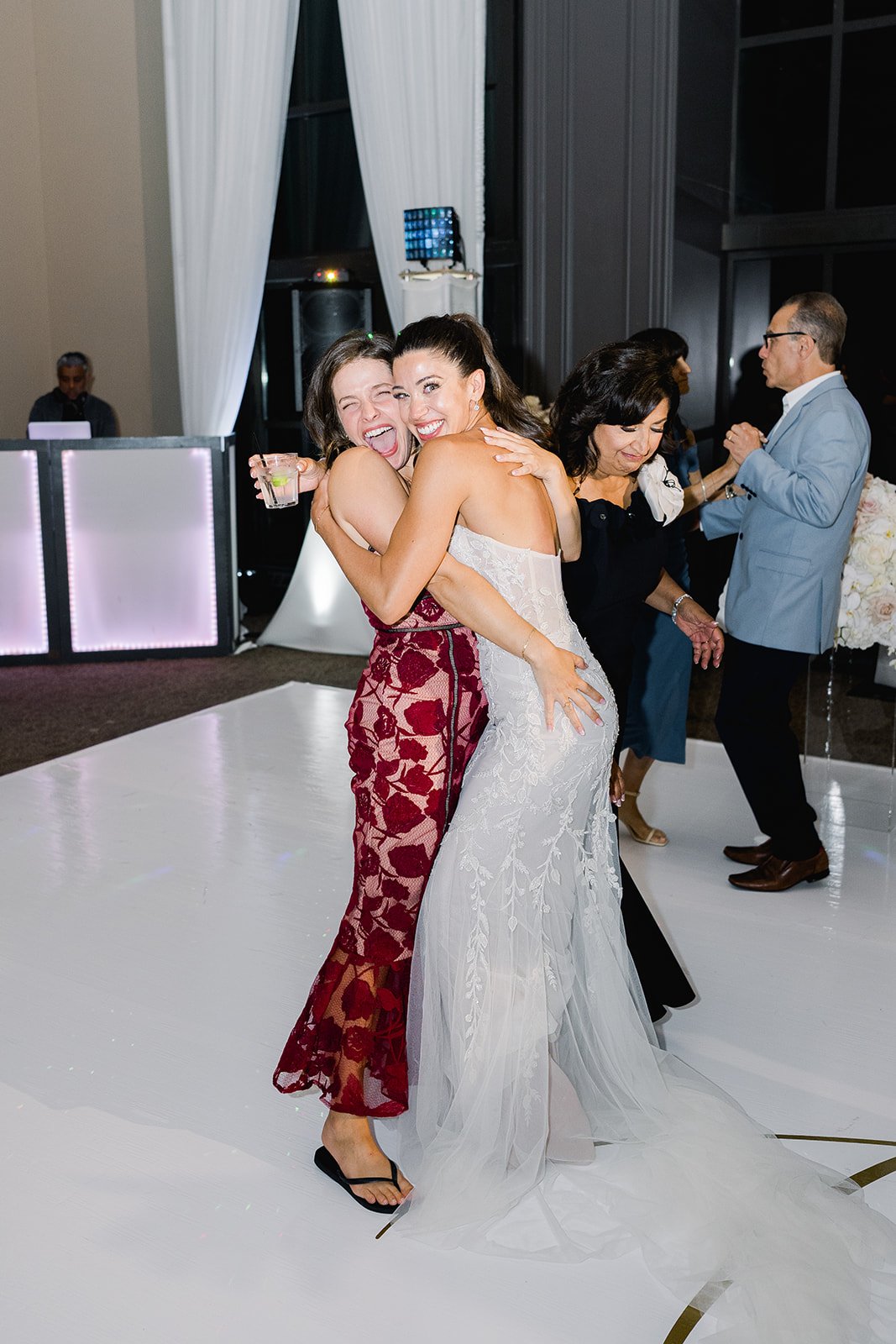 A beautiful bride hugs her friend on the dancefloor of her wedding.