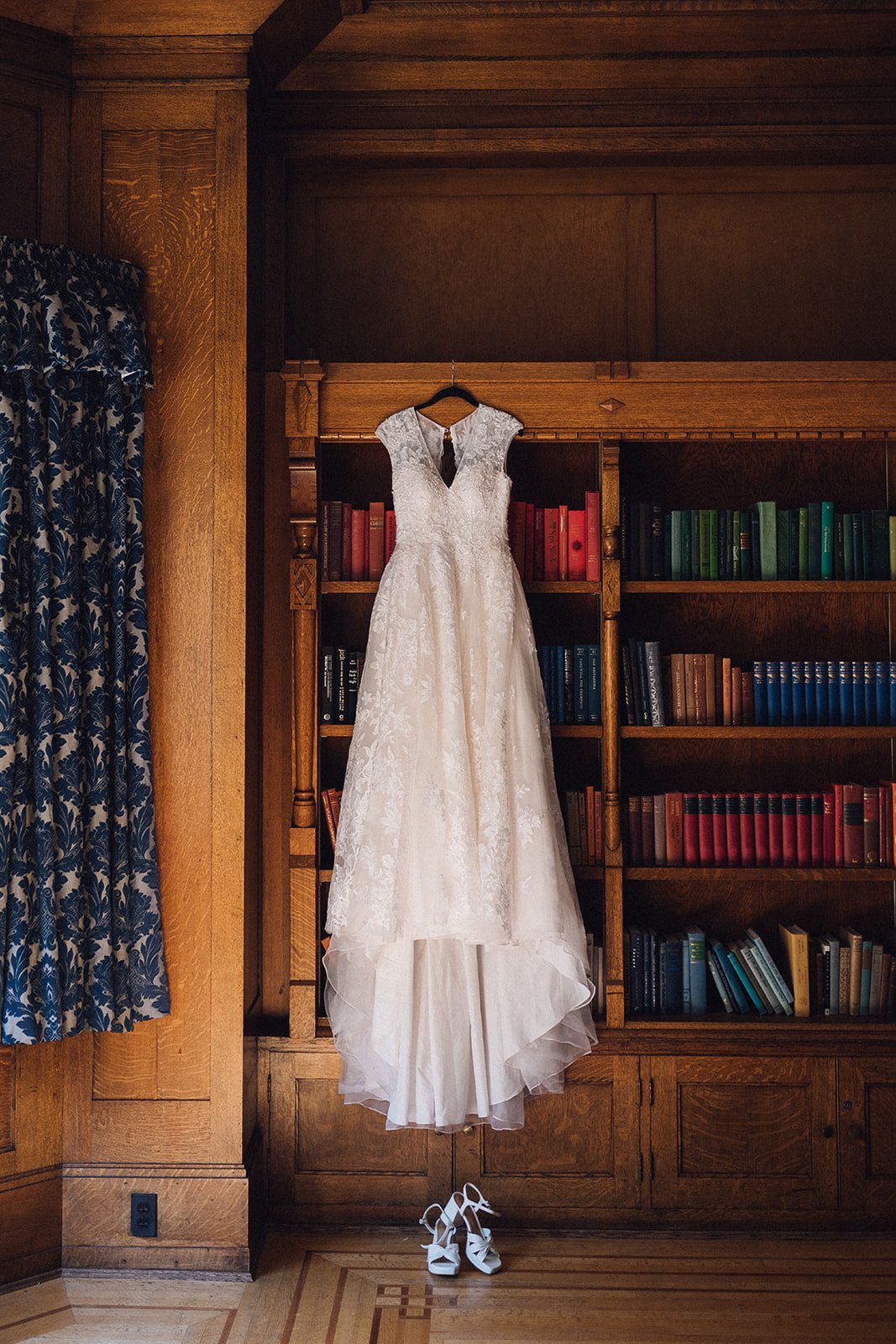 Lace wedding dress hanging from antique wooden bookshelf at Cecil Green Park House in Vancouver, BC.