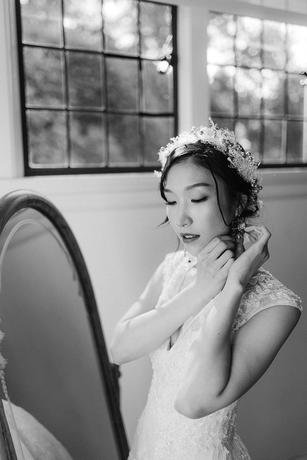 asian bride putting on her earrings while looking in the mirror at Cecil Green Park House. Beautiful Life Studios BC.