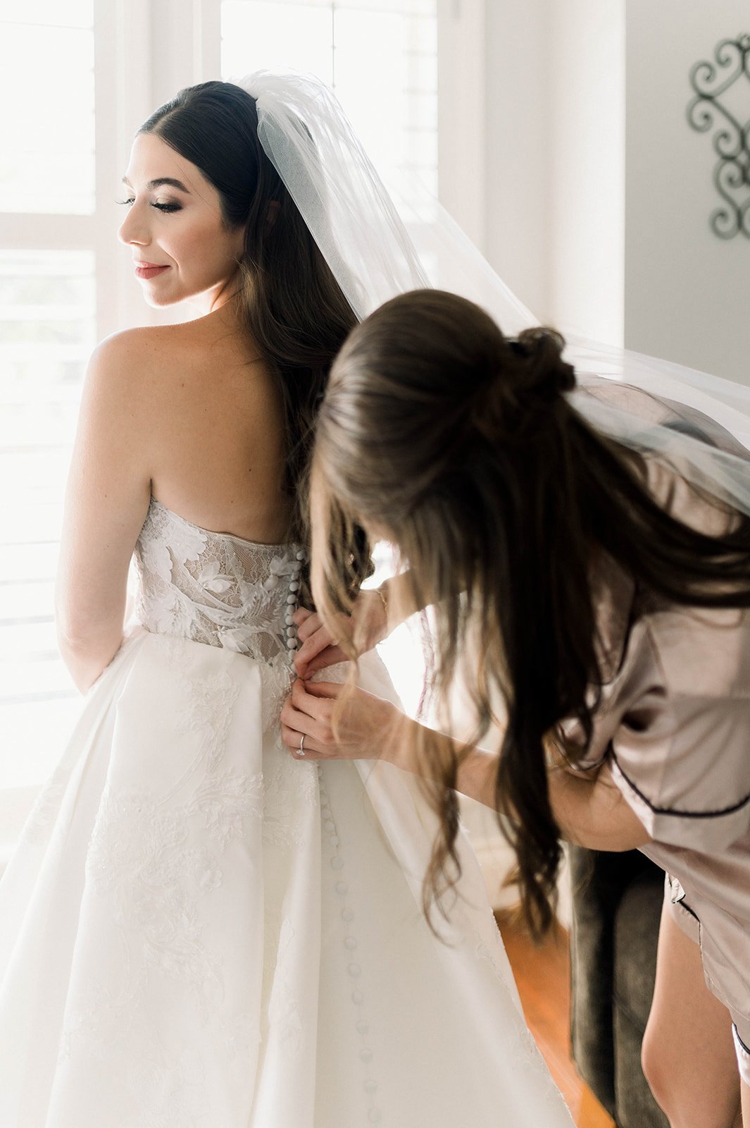 Sister of Bride meticulously fastens buttons on brides sexy wedding dress 