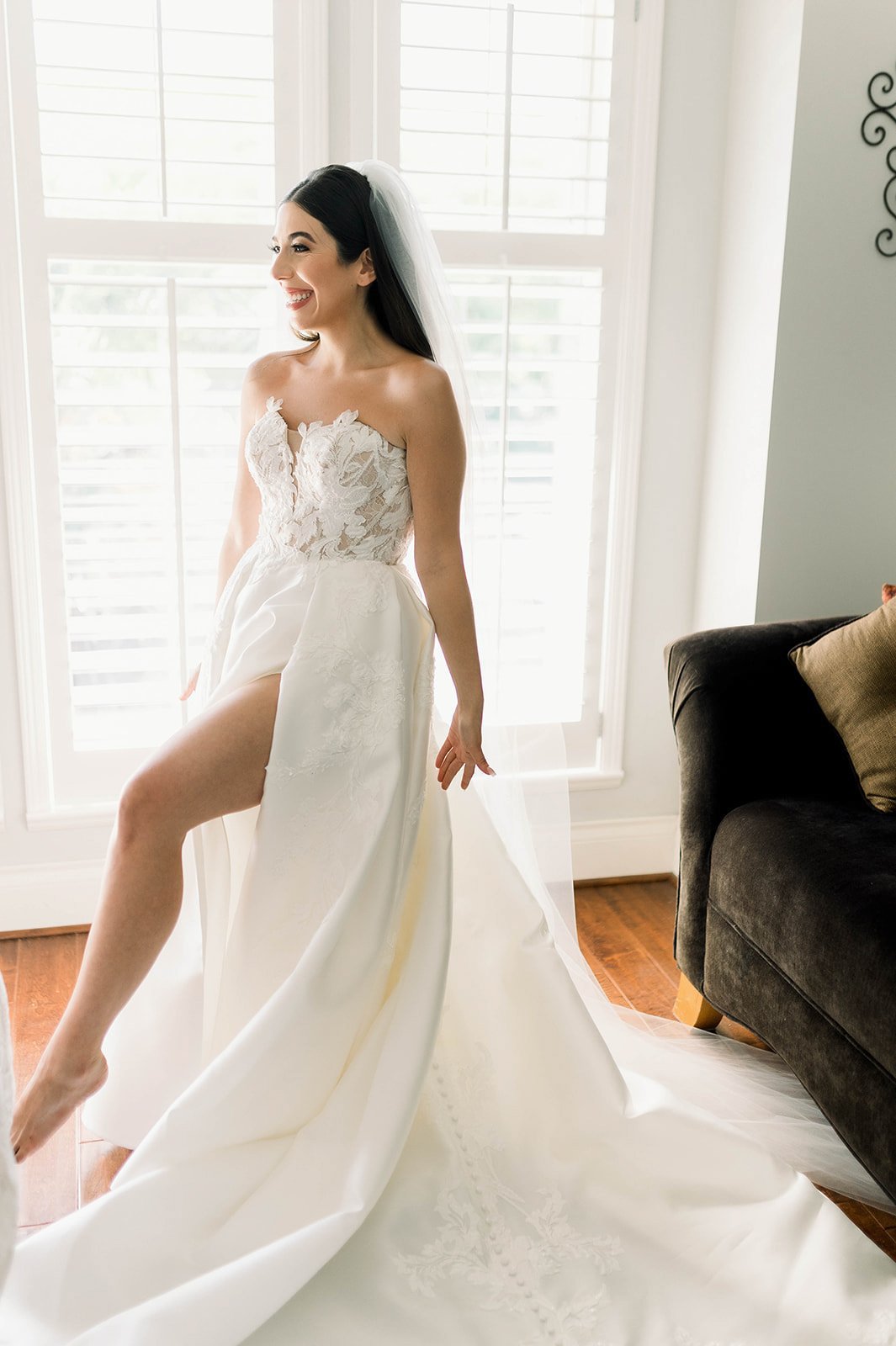 Bride poses in sexy wedding dress with leg slit as the morning light gently gleams through window. 