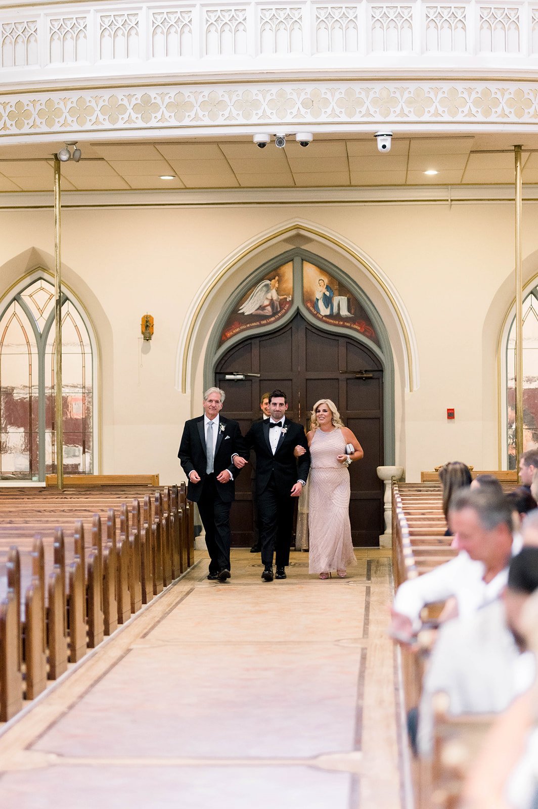 Groom is escorted down church aisle by parents during hart House wedding in Vancouver.