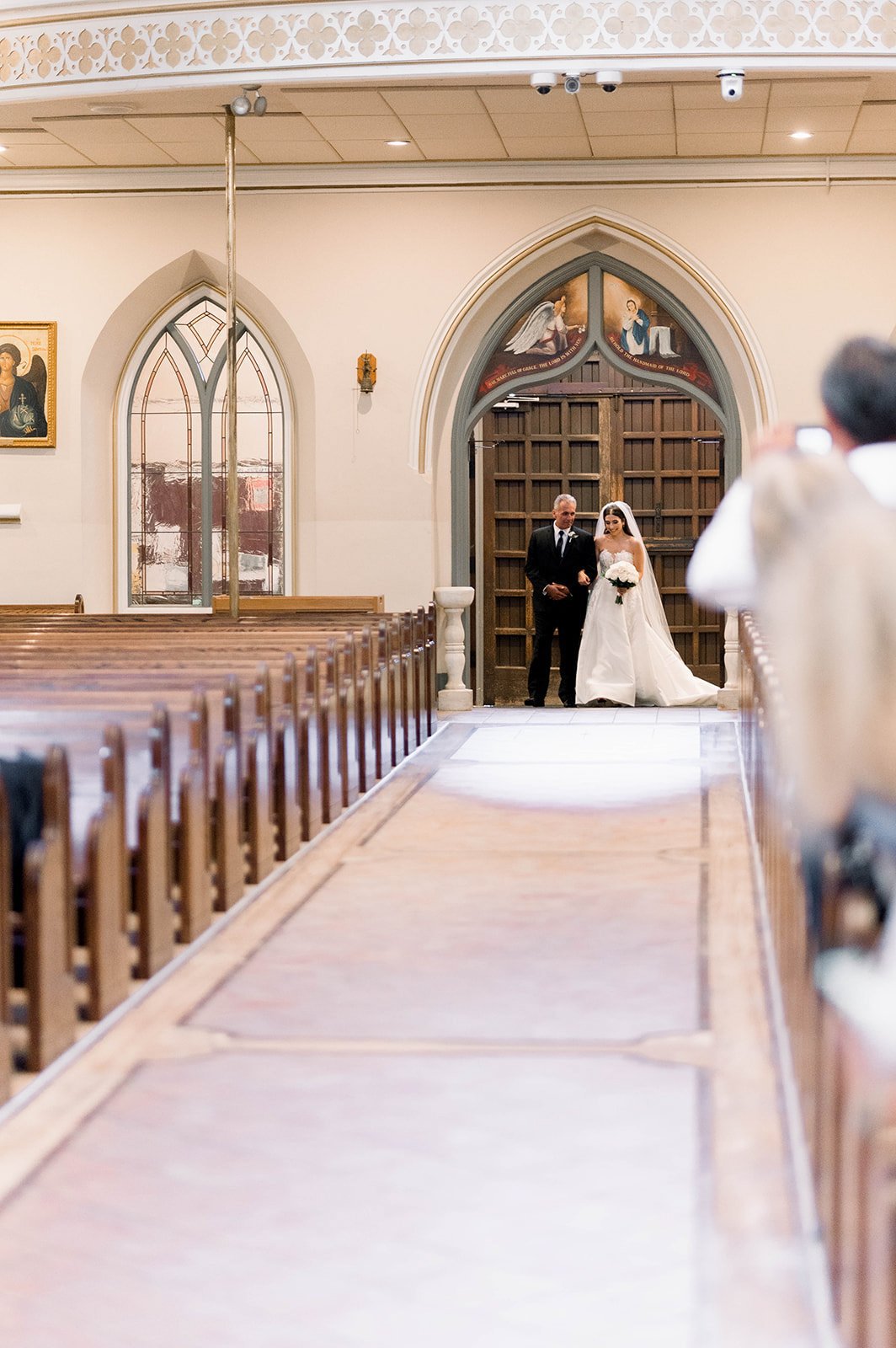 Ballgown wearing bride is escorted down long church aisle by father in Hart House Wedding.