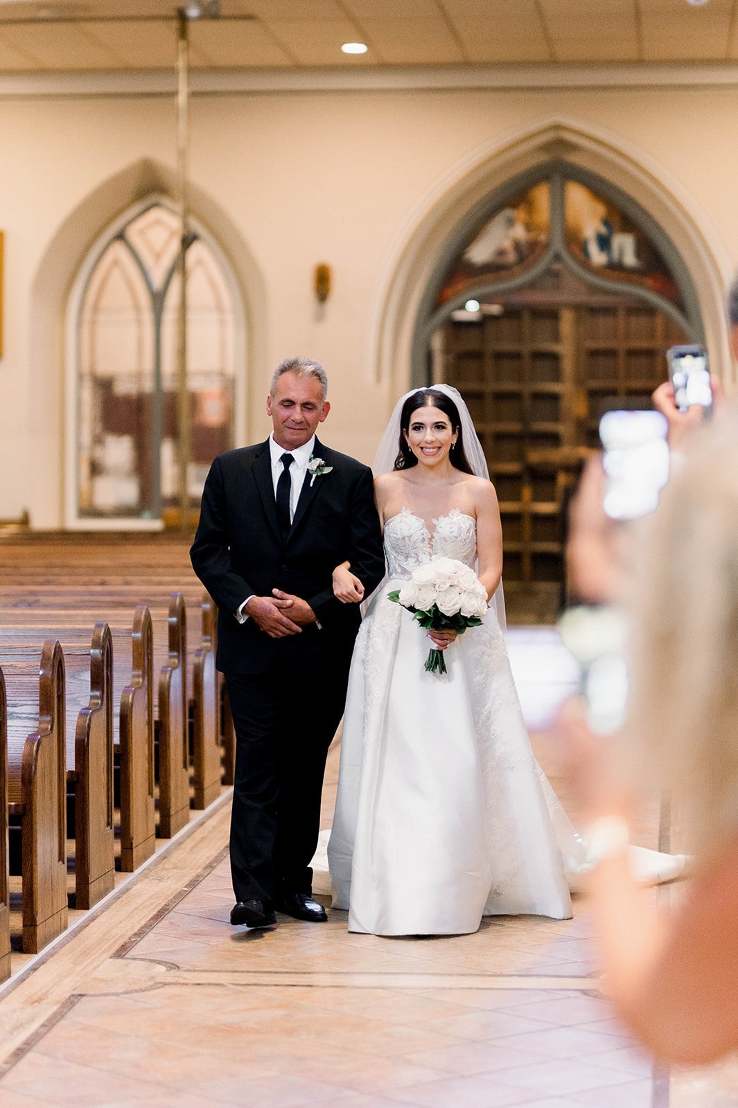 Bride walks down aisle with her father in large catholic church in Vancouver BC