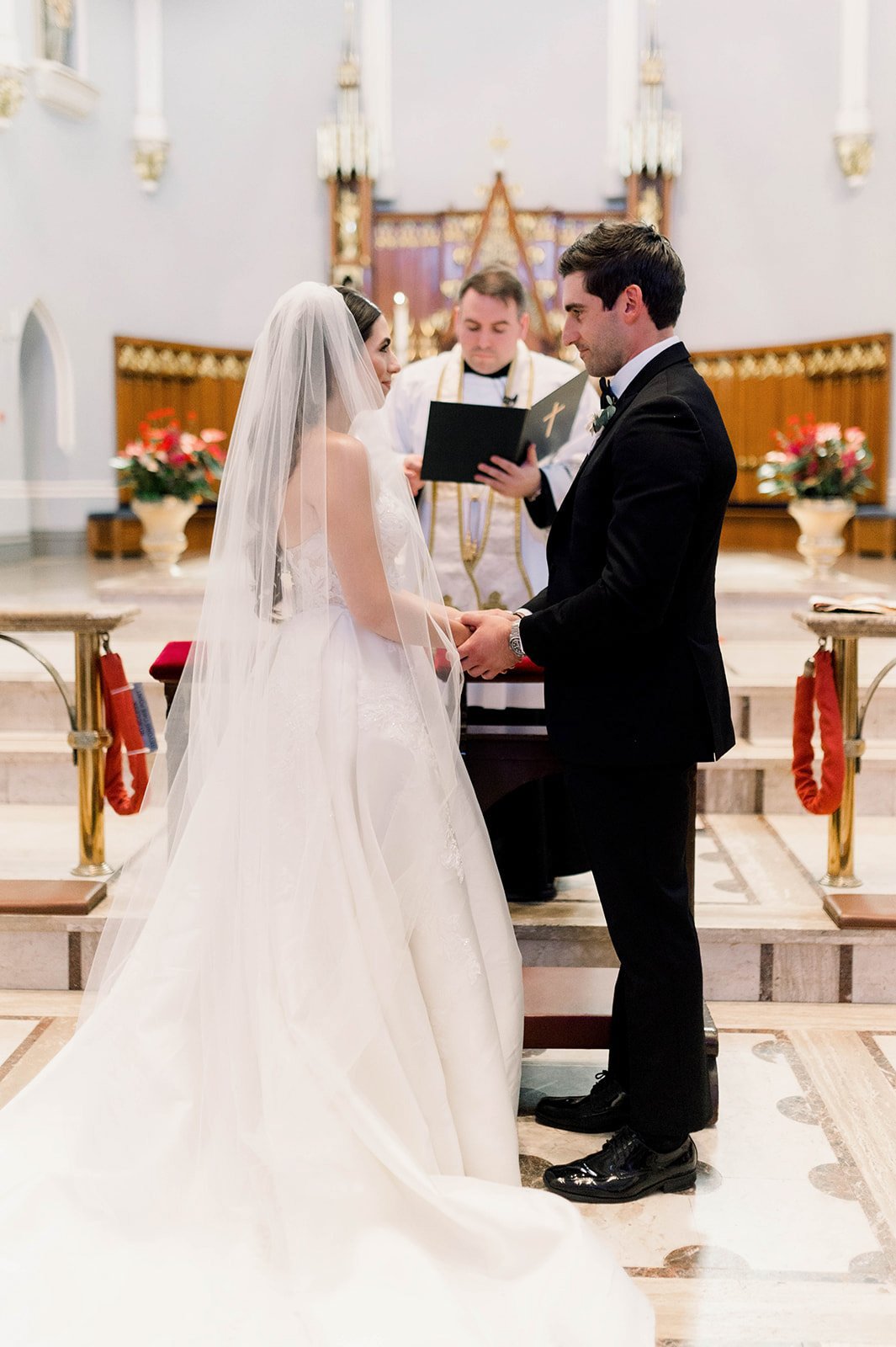 Beautiful bride and handsome groom hold hands as they exchange vows in traditional ceremony in a catholic church in Vancouver, British Columbia.