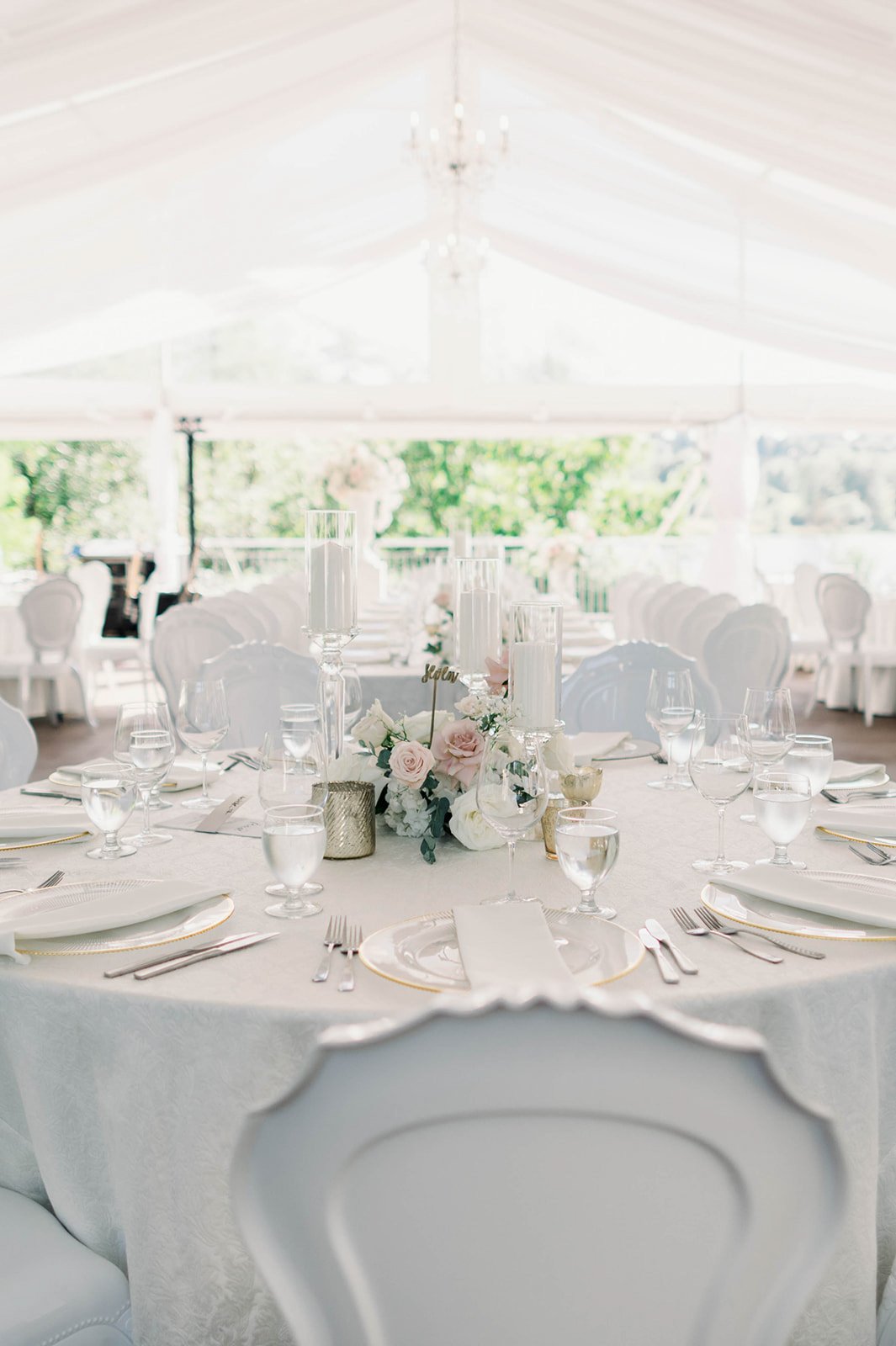 Beautiful floral arrangement and decorative plates sit atop crisp white linens inside Hart House wedding tent.  