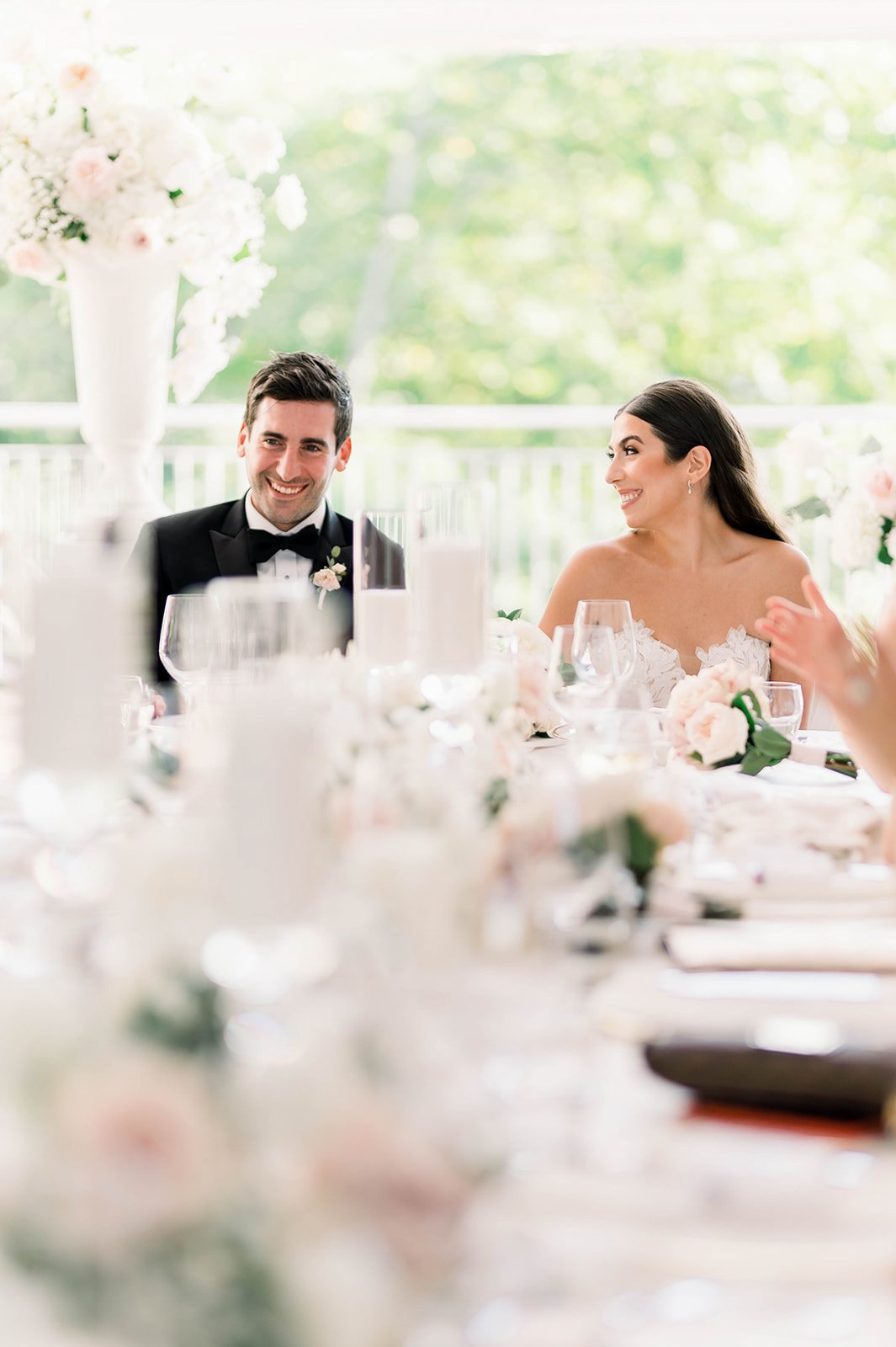 Bride and groom laugh, surrounded by flowers and candles at head table in Hart House. 