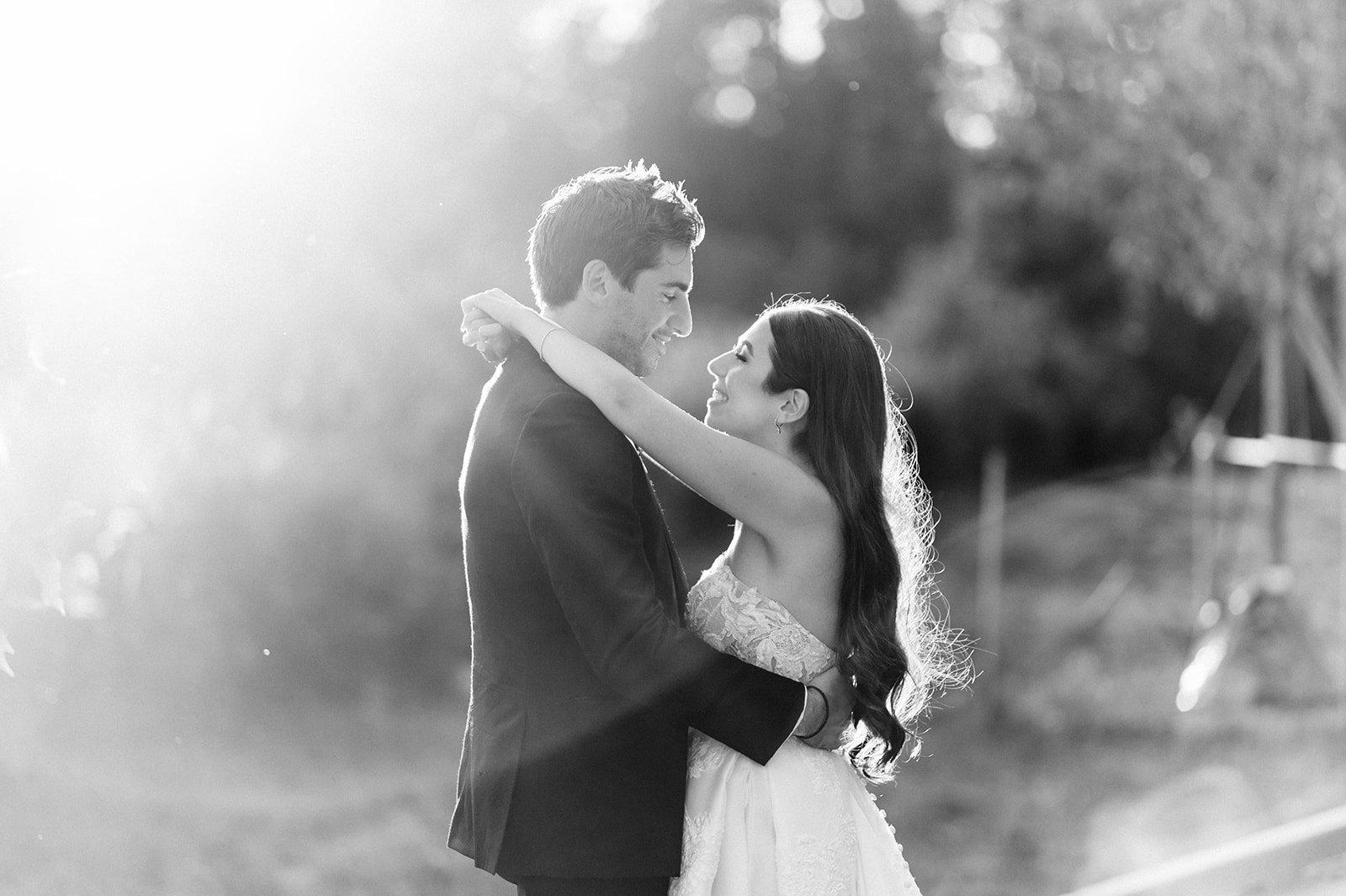 Bride envelops groom in loving embrace as a beautiful sunset flares into lens at hart house.  