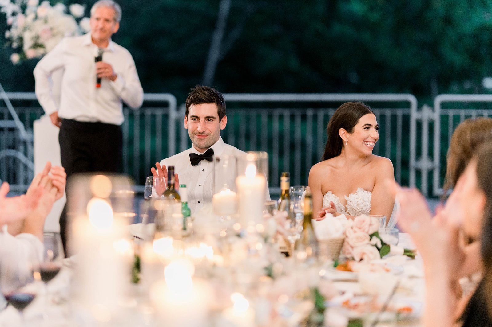 Bride and groom grin at wedding guests while seated at their head table during a Hart House reception.