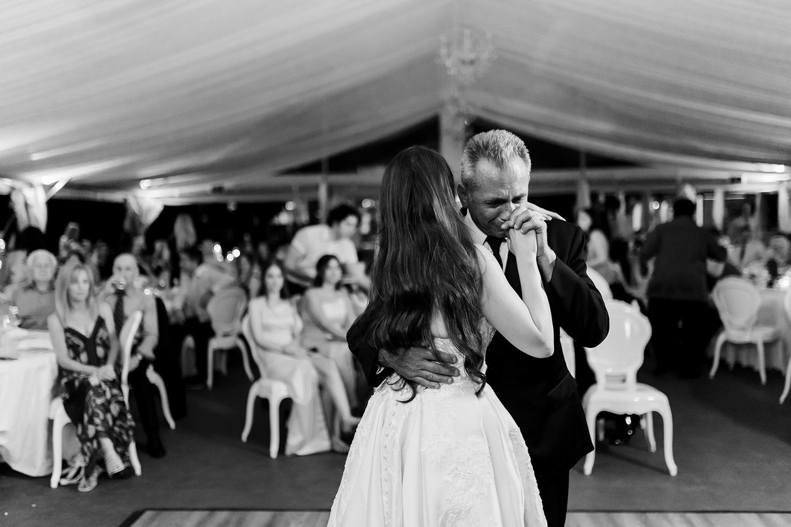 Groom kisses Brides hand as they slow dance and wedding guest on-look at Hart House. 