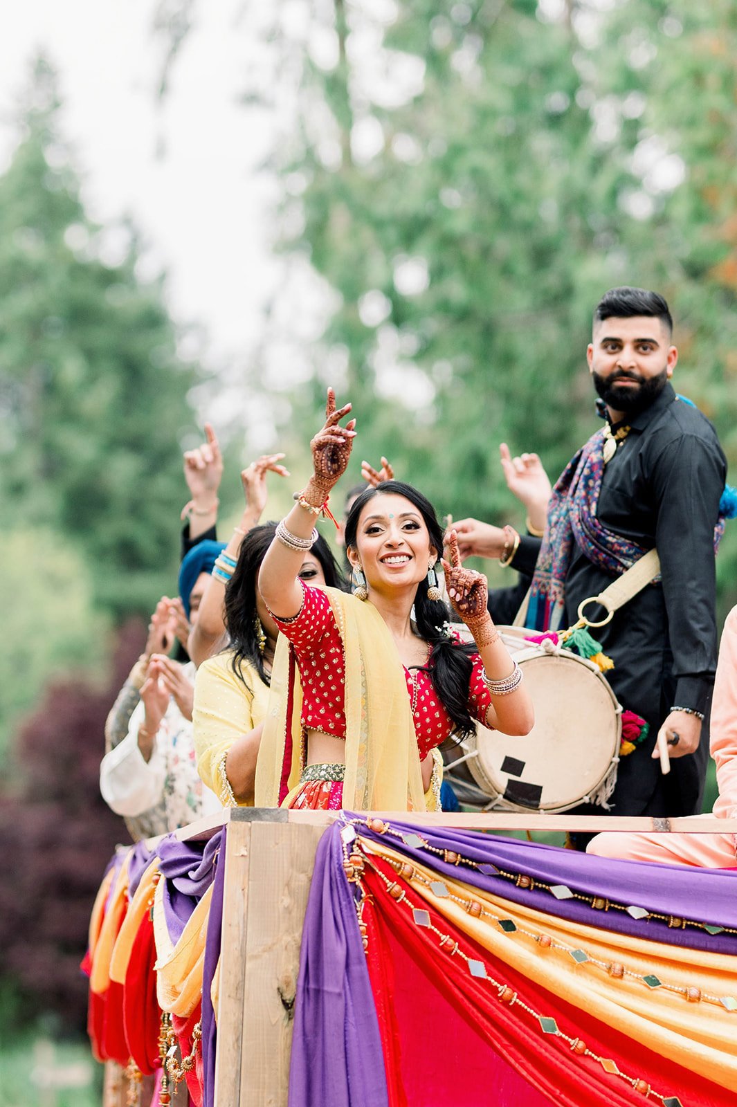 South Asian Bride waves to camera in a pink and yellow lehenga choli set at her mayian ceremony.