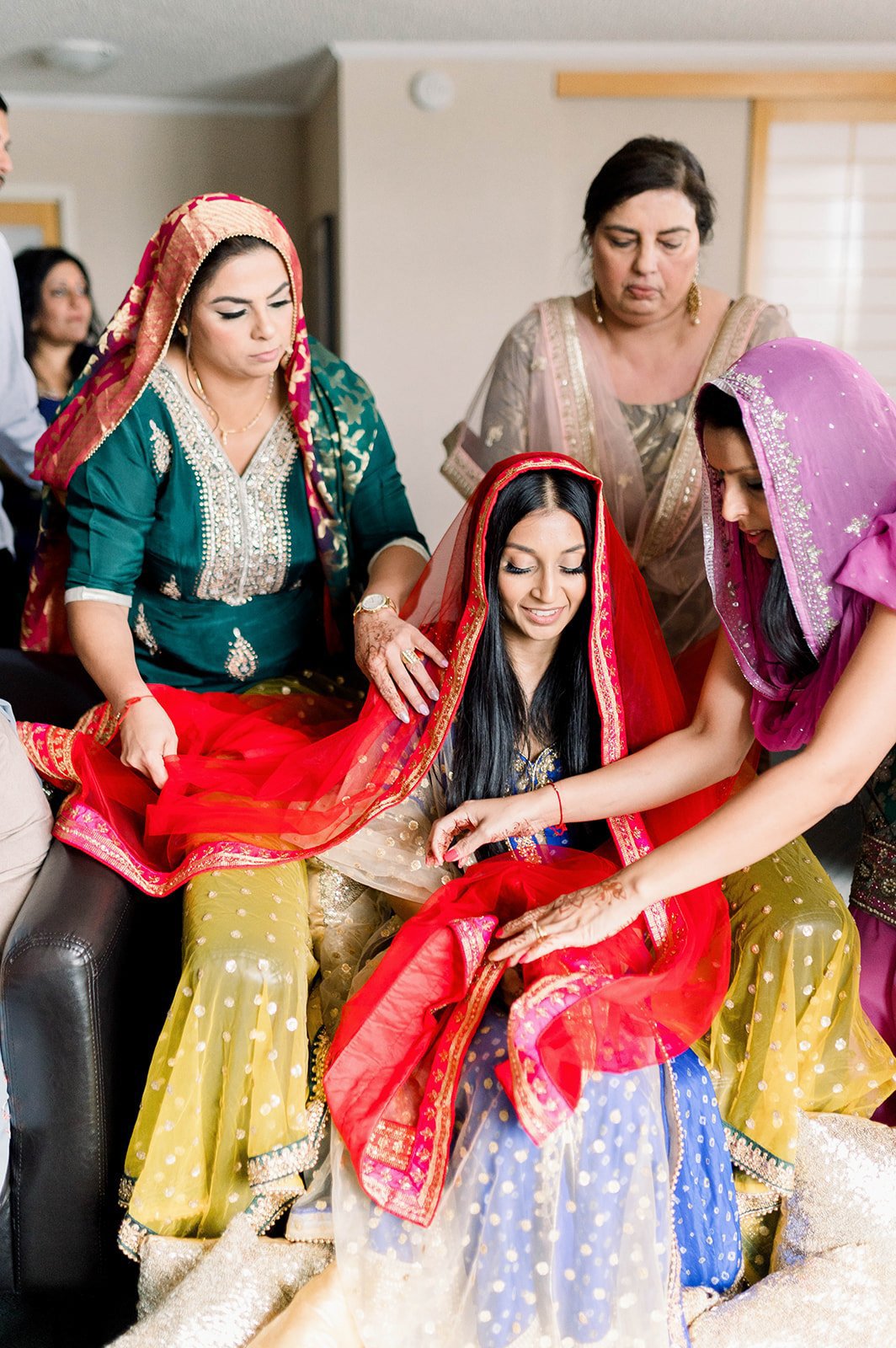 An Indian Bride is covered in a red Chunni before her Indian Wedding.