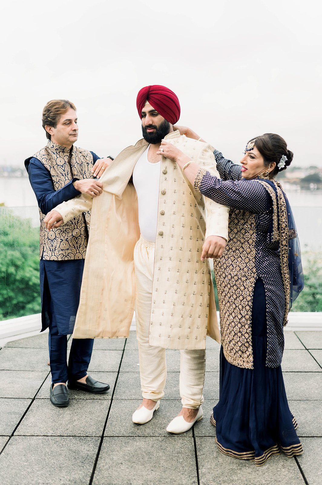 The mother and father of the groom help him into his wedding day tunic before his traditional south asian ceremony 