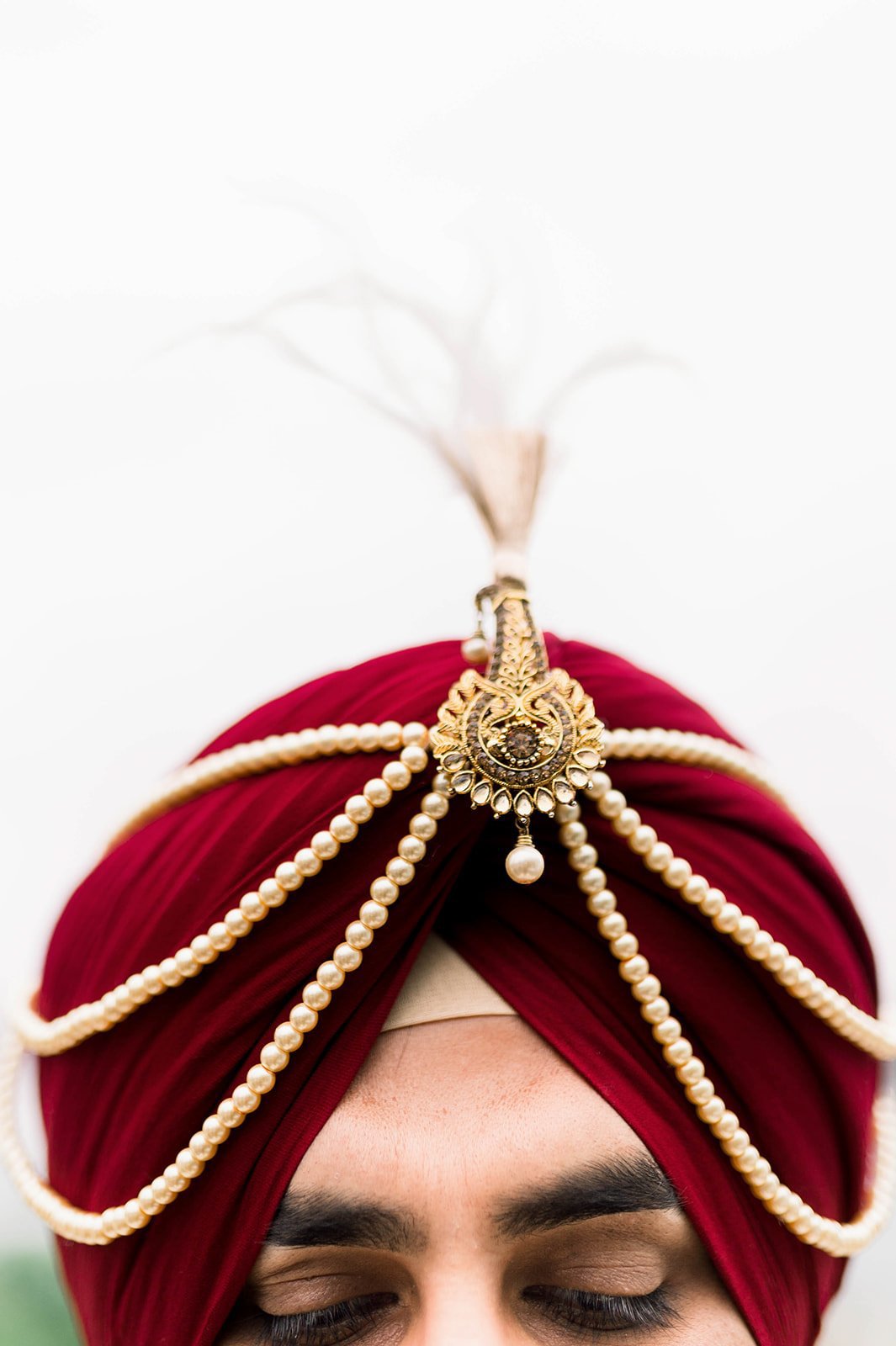 A gold Kalgi adorns a red turban on a South asian groom 