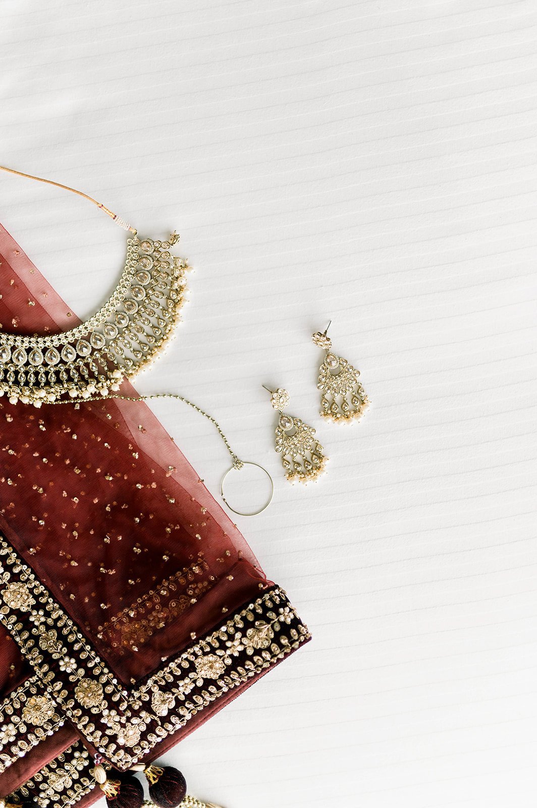 A gold necklace sits atop a red bridal chunni next to gold earrings. 