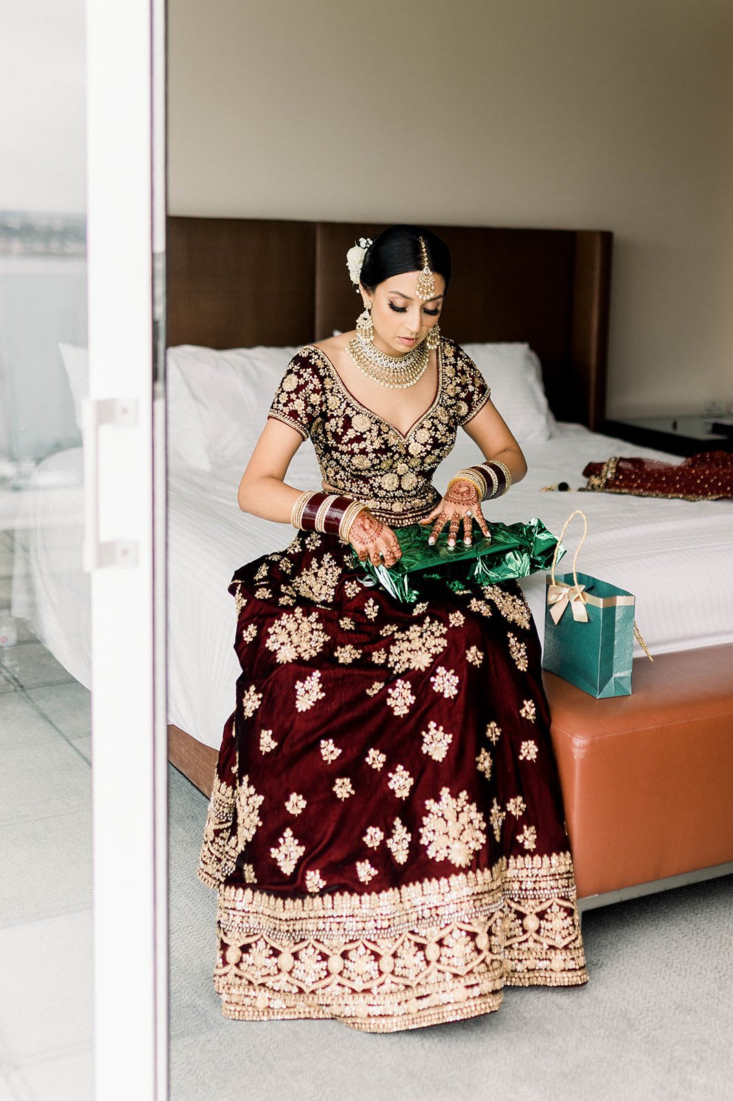 An indian bride in a traditional red and gold lehenga opens a present from her groom on her wedding morning in Victoria BC 