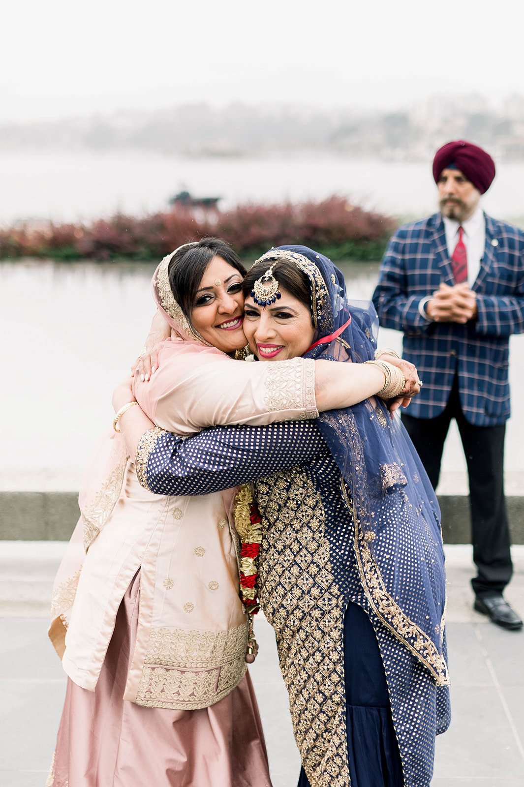 Two moms hug while smiling towards the camera during a Sikh milni in Victoria BC