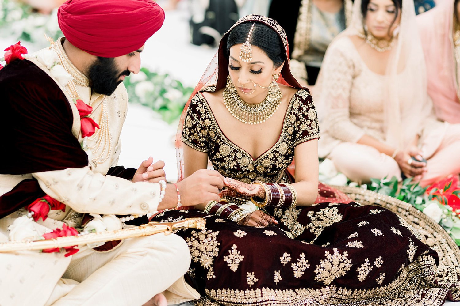 An indian bride and groom in traditional wedding attire exchange wedding bands.