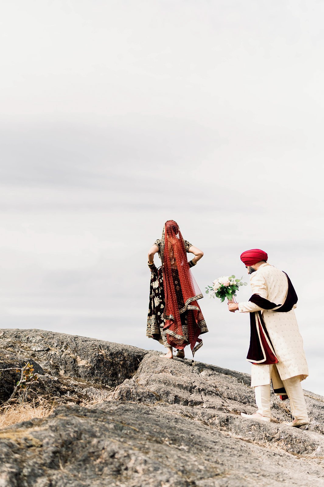 An Indian bride holds up her lengha as she leads her groom up a romantic rock formations.