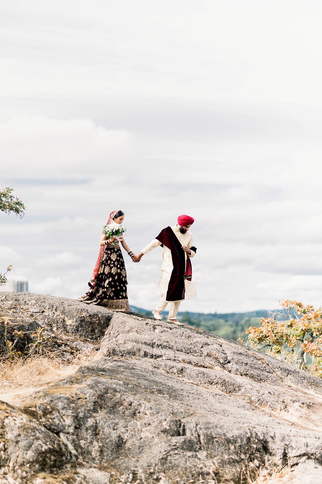 An Indian groom leads his bride down a rock formation at the end of their photoshoot in Victoria BC