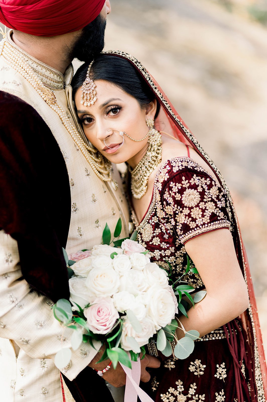 An Indian bride stares into the camera as she rests her head on her groom's chest.