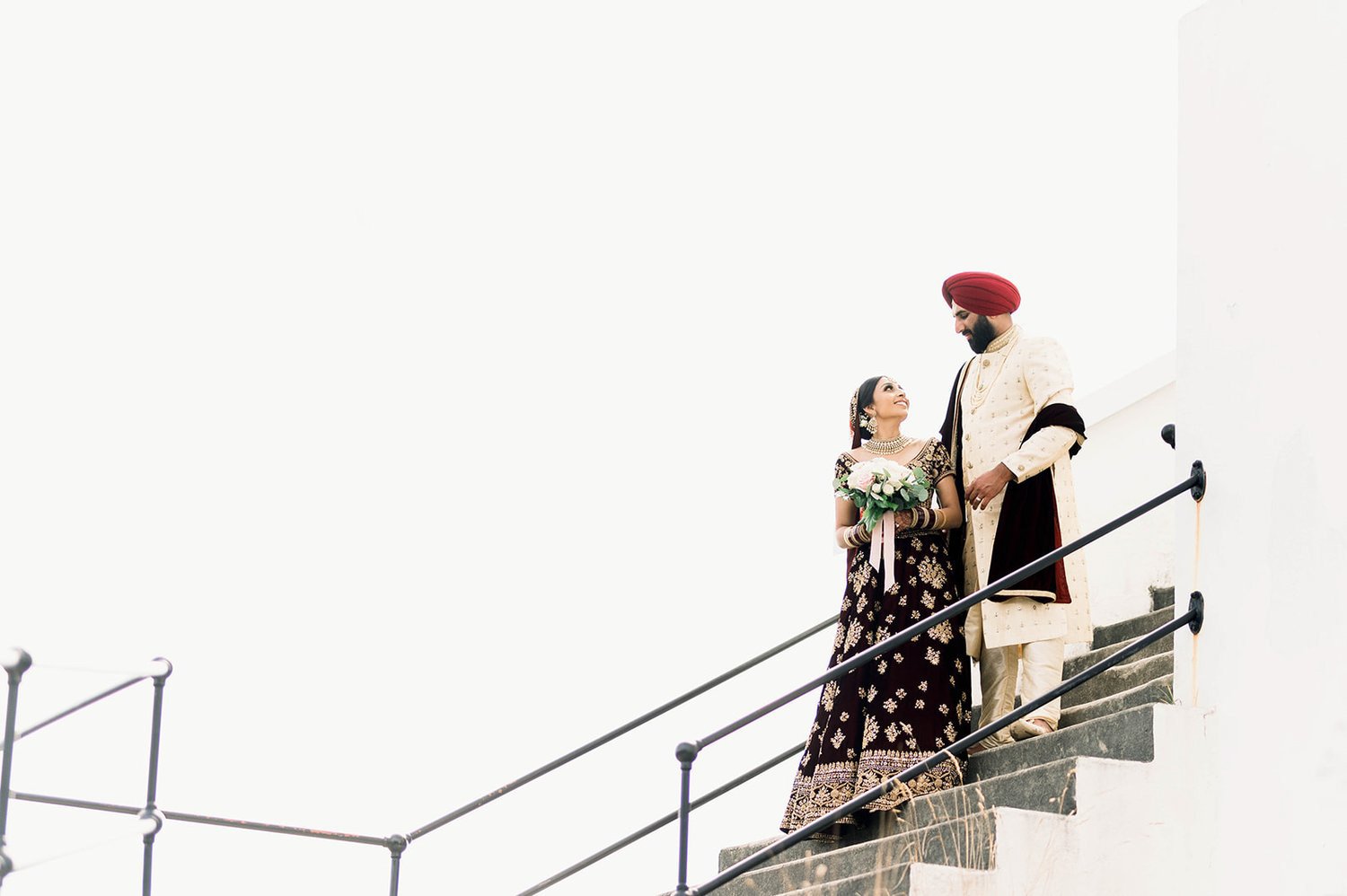 A bride and groom descend a concrete staircase. 
