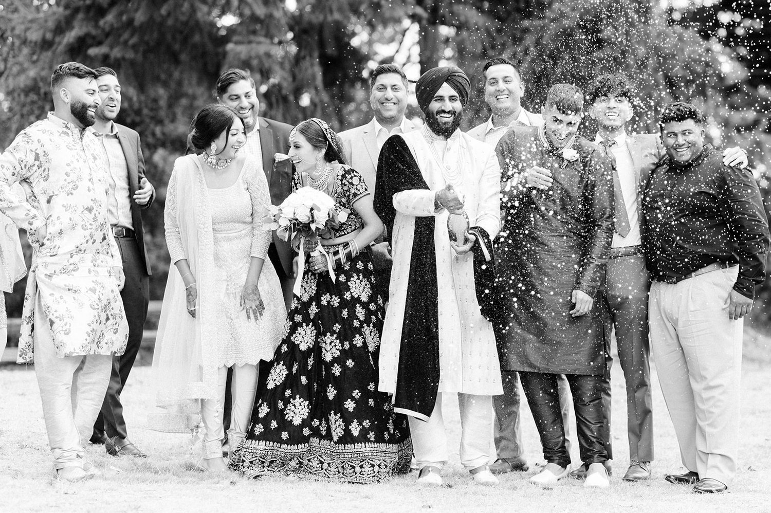 An indian groom smiles as he pops champagne surrounded by his wedding party in Victoria BC. 