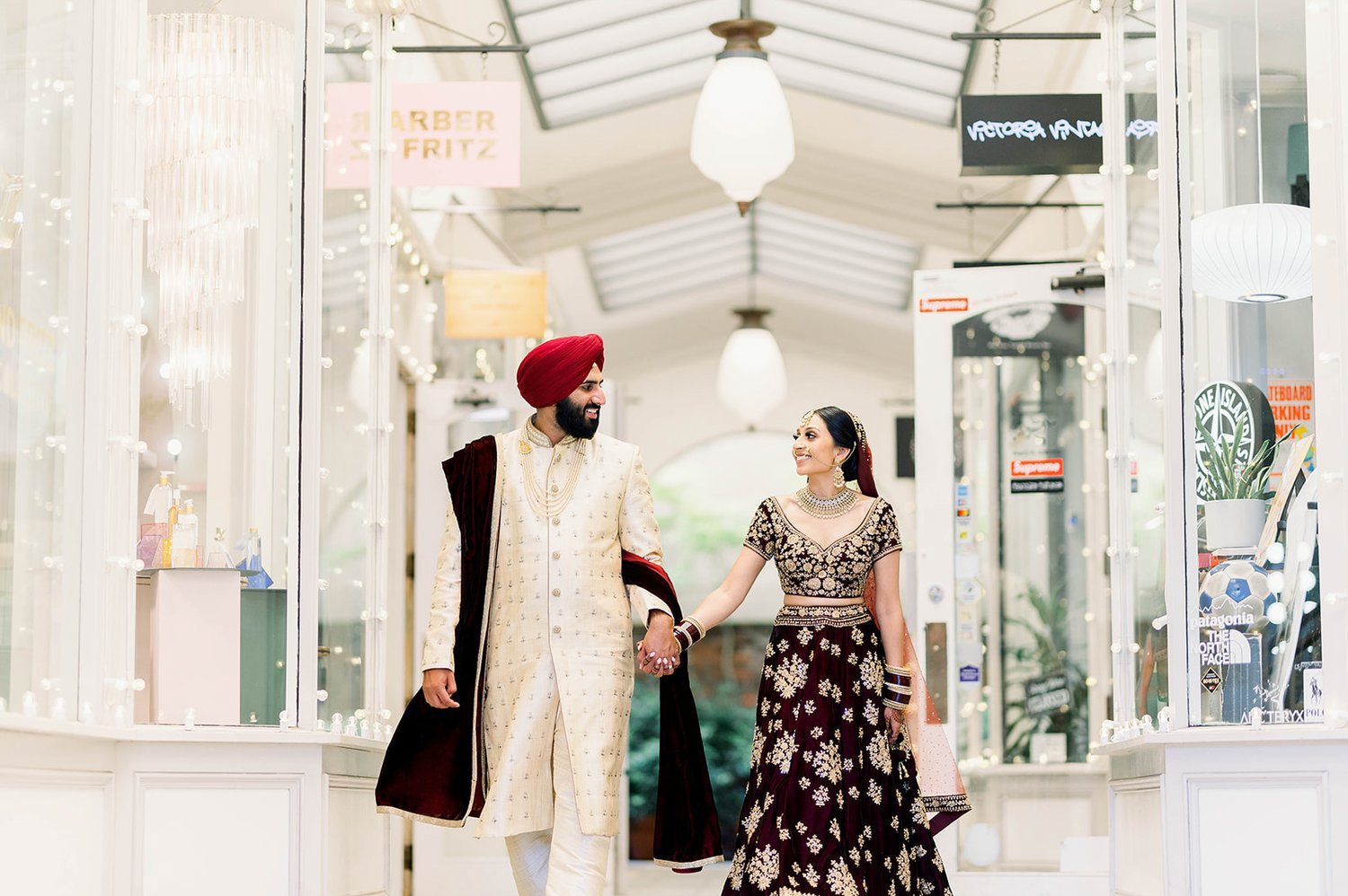 An indian bride and groom walk hand in hand towards their reception. 