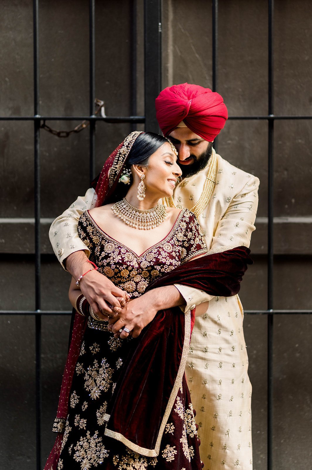 A South Asian groom hugs his bride from behind as she smiles in Victoria BC. 