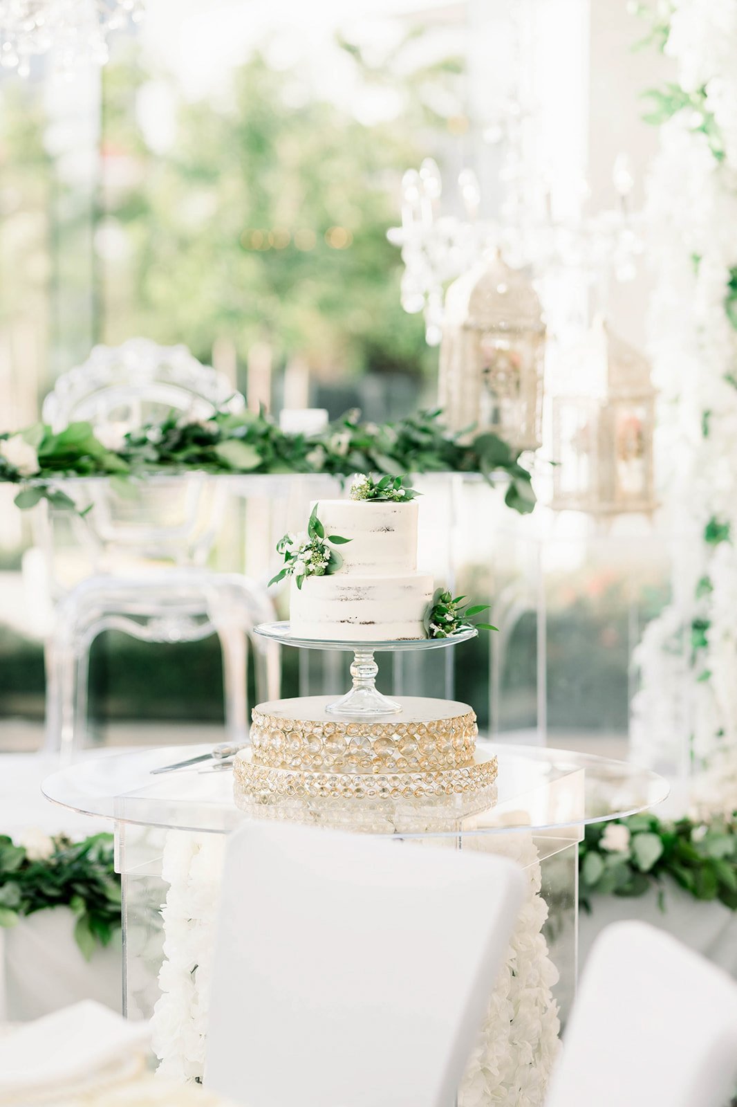 A white wedding cake is decorated with green leaves in a reception space.