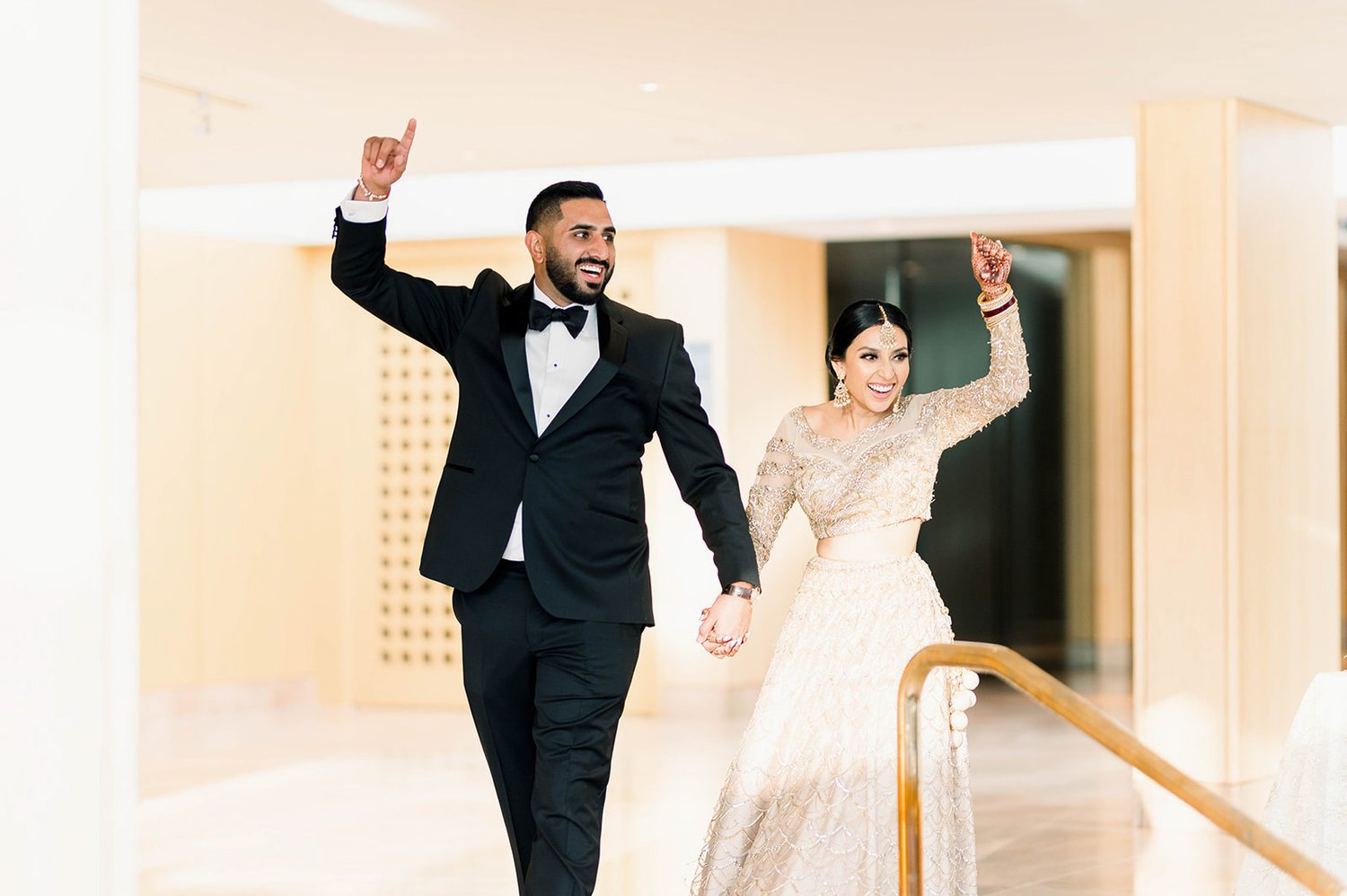 A bride and groom enter their reception in a grand entrance, hands held aloft.