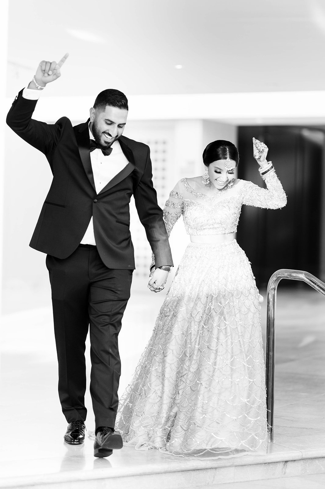A black and white photo of an indian couple celebrating as they enter their reception. 