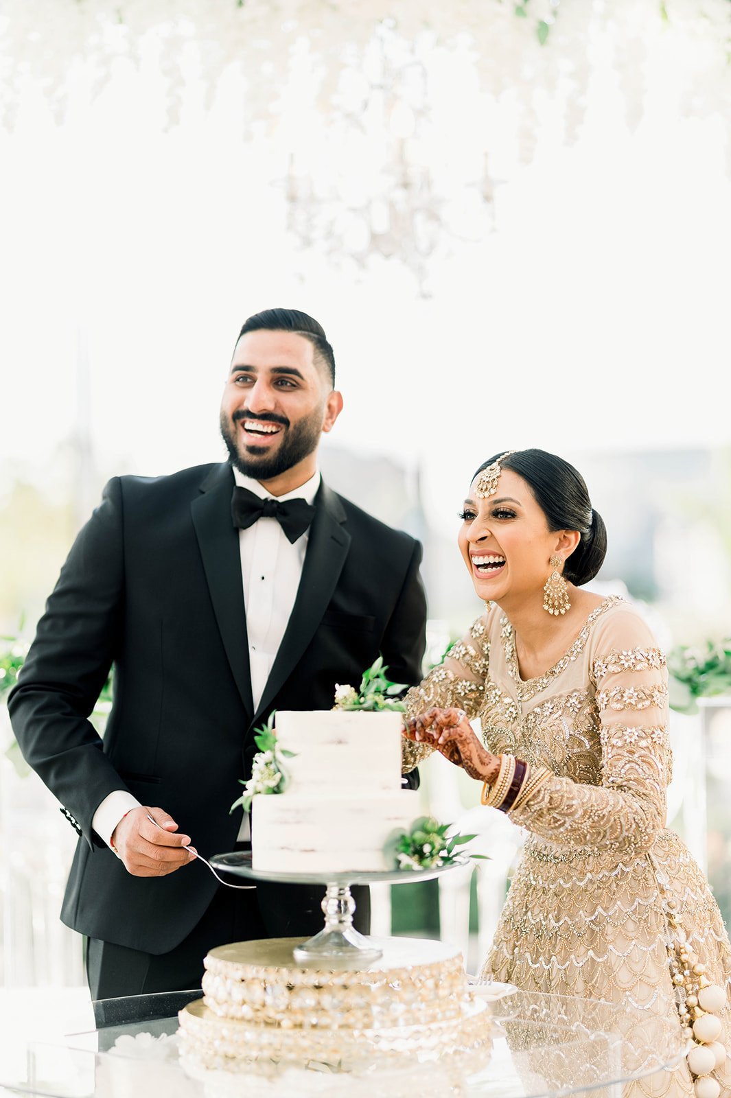 An indian couple smile and laugh as they cut their wedding cake in Victoria BC. 