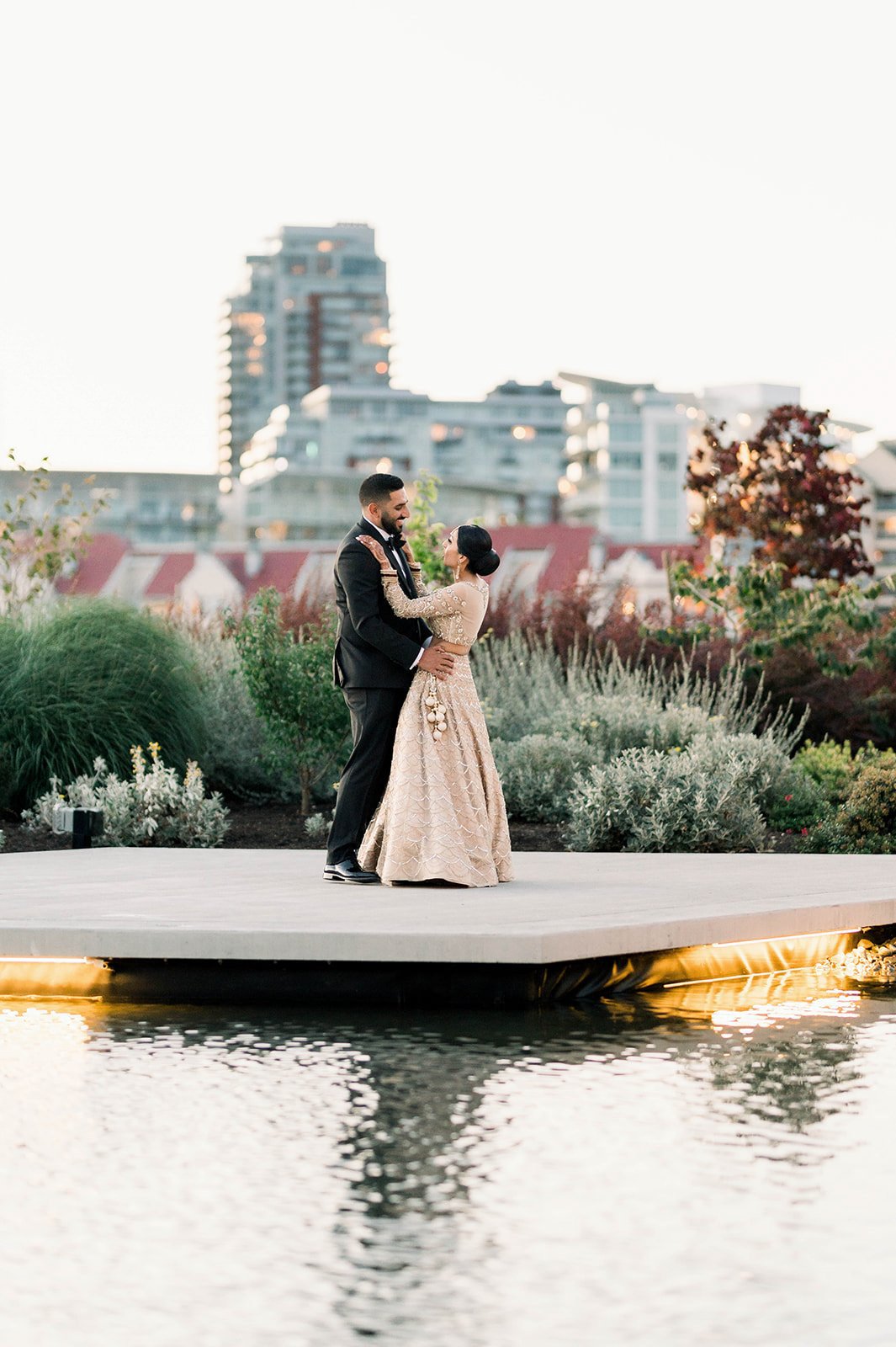 An Indian groom in a black suit and a bride in a gold lehenga dance on a boat dock in Victoria BC.