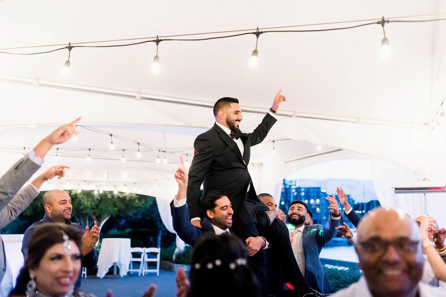 An indian groom is lifted onto the shoulders of his family as they dance at his reception.