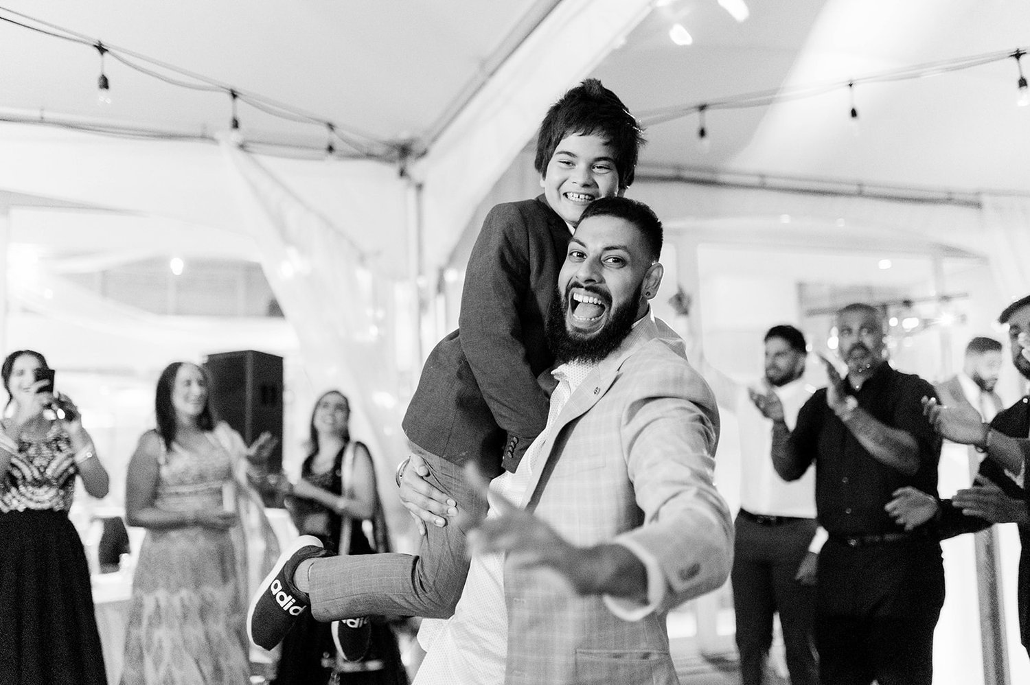 A father and son laugh as the father lifts his son on the dancefloor.
