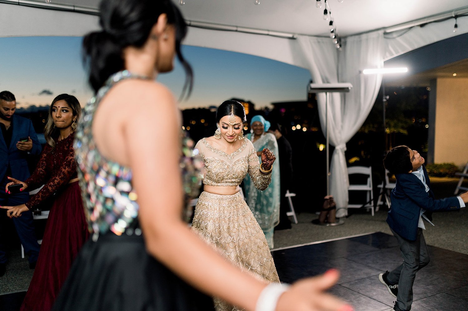 An indian bride in a gold lehenga dances in a tent during her reception.