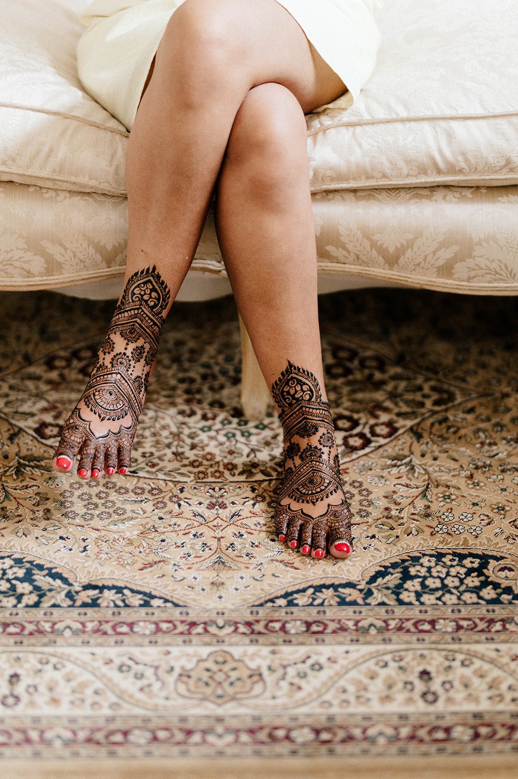 A woman shows off her bridal mehndi by crossing her legs on a couch. 