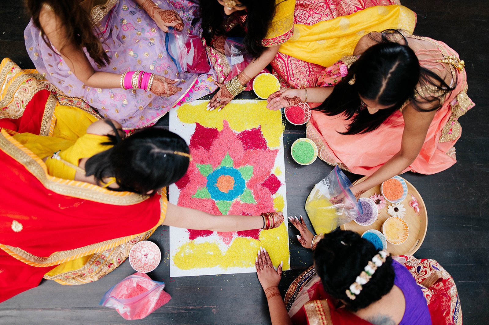 A group of women apply rice to a colourful bright rangoli board in surrey bc 