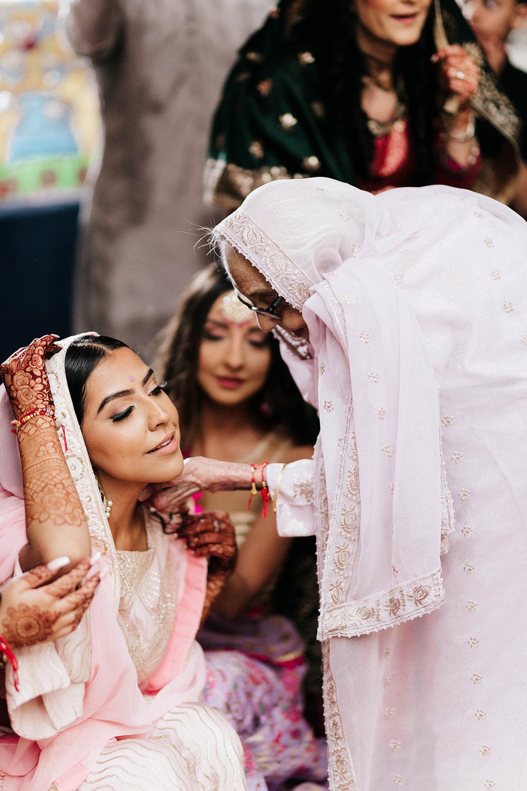 A brides grandmother applies turmeric paste to the brides face in her maiyan ceremony 