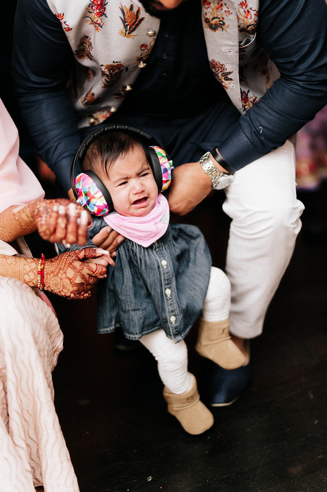 A baby in earmuffs cries as her family tries to get her to pose for a photograph. 