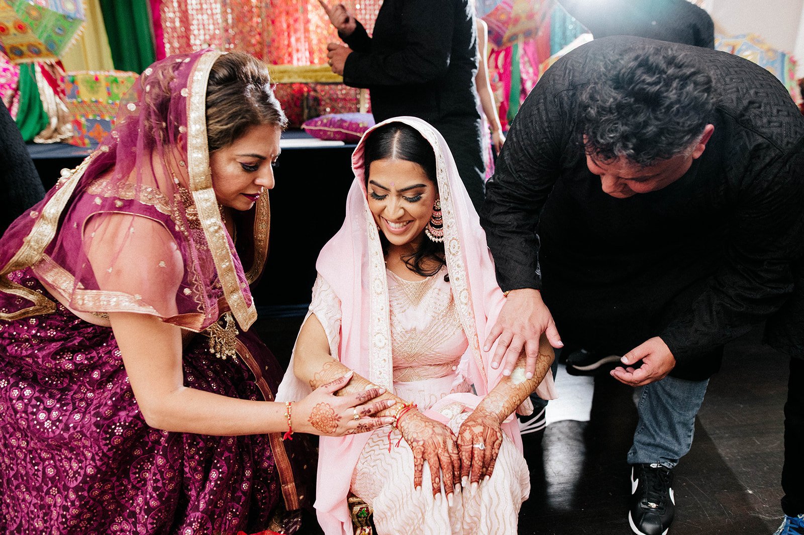 An indian bride smiles as relatives as friends apply maiyan paste to her arms in Surrey BC 