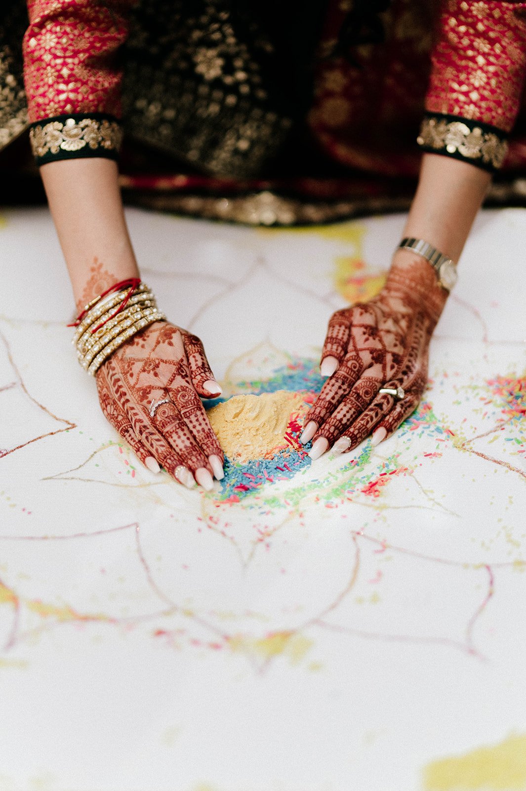 hands coved in henna designs scoops rice off of an rangoli board