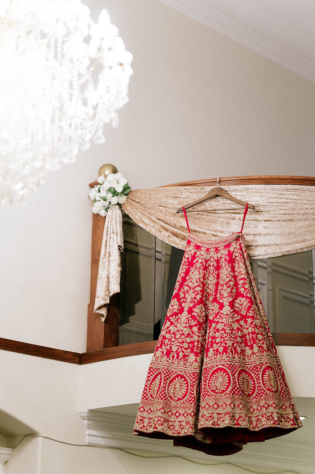 A red bridal lehenga hangs from a loft, next to a chandelier 