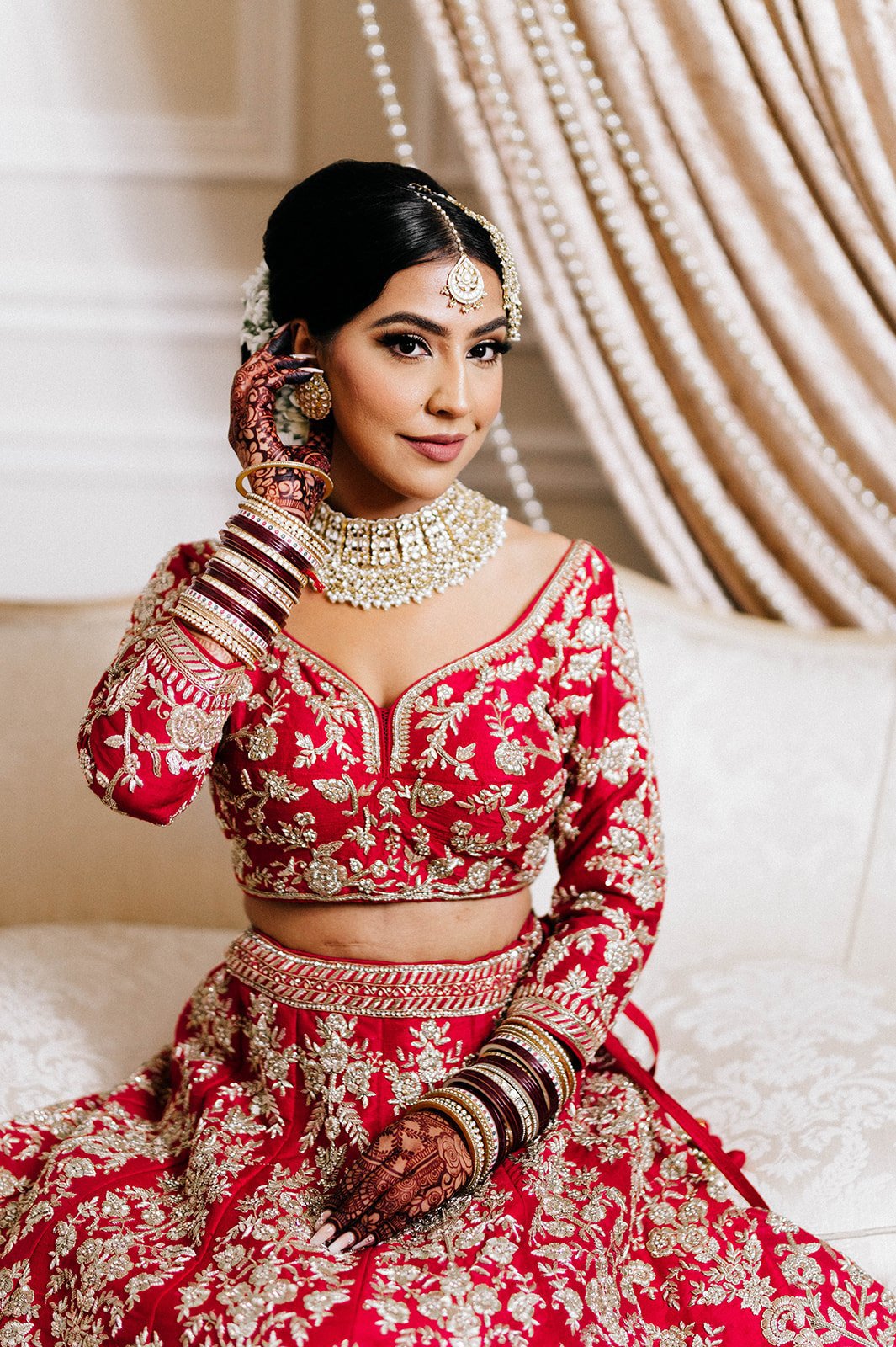 A beautiful indian bride smiles as she adjusts her hair as she gets ready for her wedding.