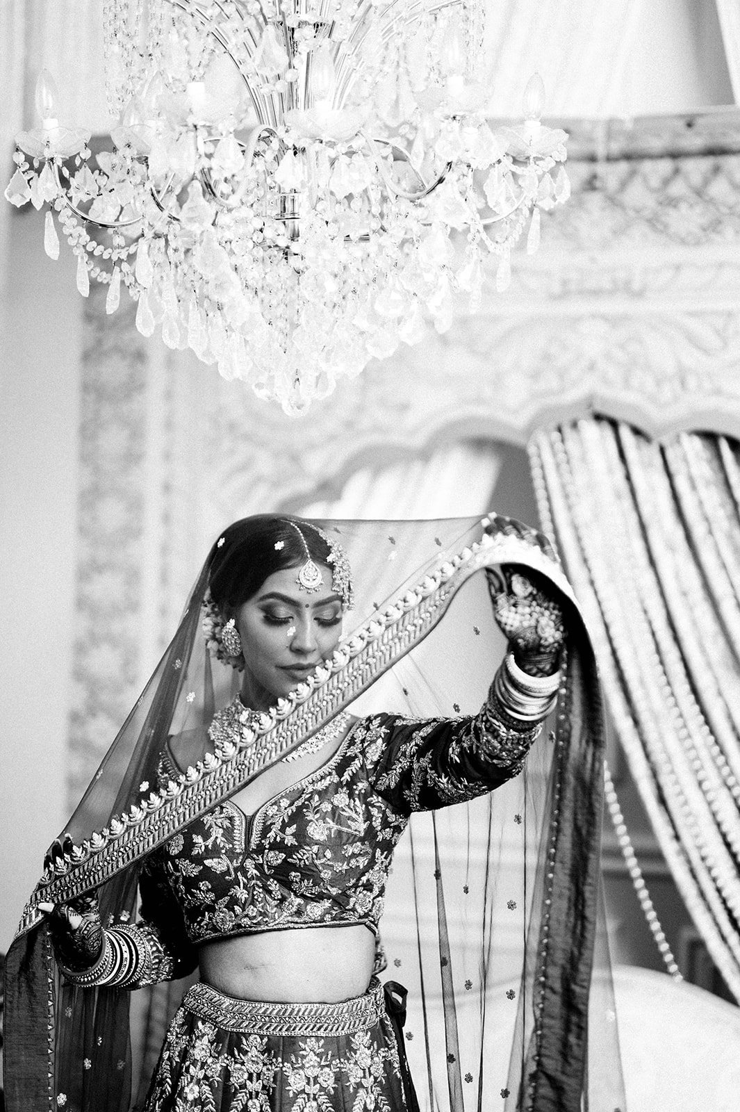 A bride adjust her her chunni as she poses for a black and white photograph
