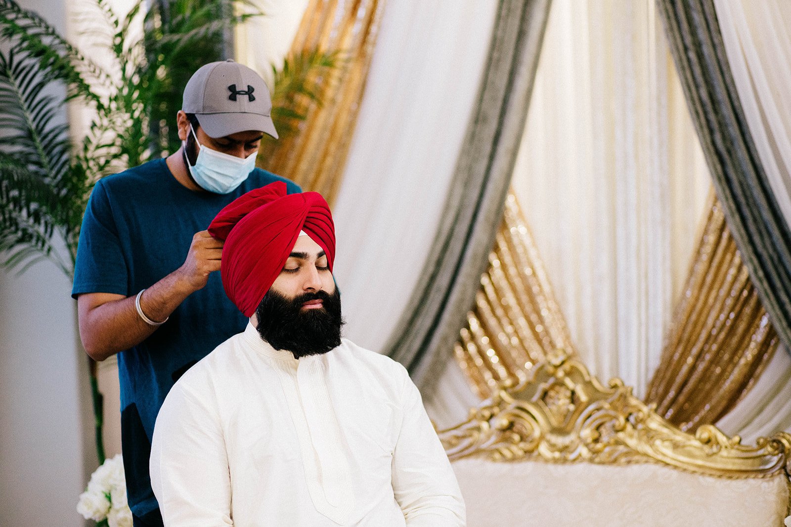 A south Asian groom has his red turban tied on his wedding morning